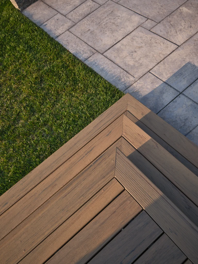 Close-up of precision mitered deck boards with a clean transition to a stone patio and lawn.